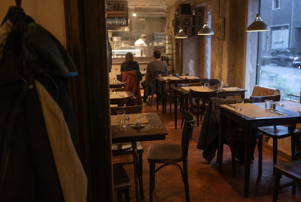 Blick in die Gaststube am Abend: gedeckte Holztische, Bugholzst&uuml;hle und Jacken an der Garderobe