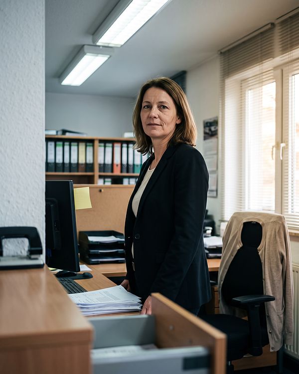 Julia Wiegmann an ihrem Schreibtisch im Büro, hinter ihr ein Regal mit Ordnern, am Bildschirmrand klebt ein Notizzettel