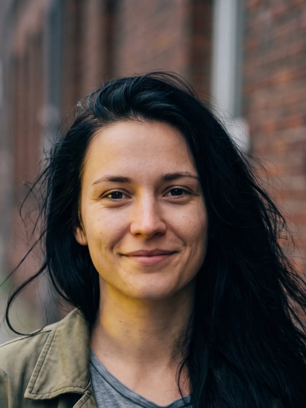 Portrait von Nadine, Fahrsch&uuml;lerin, vor einer Backsteinwand auf dem Gehweg.