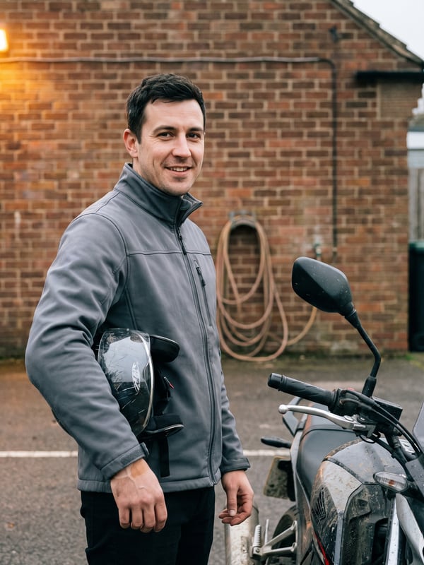Tolga Demir steht mit dem Helm unter dem Arm neben dem Schulmotorrad auf dem Hof.