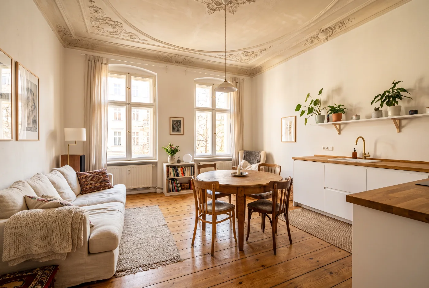 Wohnzimmer mit Leinensofa, rundem Eichentisch und offener weißer Küchenzeile mit Eichenarbeitsplatte