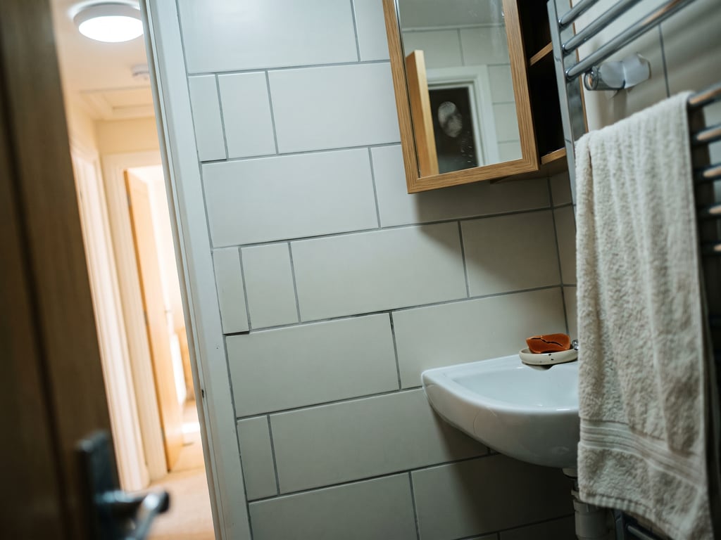 Badezimmerwand mit cremeweißen Rechteckfliesen im Verband, Handtuchhalter, Wandwaschbecken und leicht geöffnetem Spiegelschrank