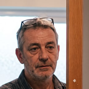 Ein Mann Mitte fünfzig mit grauen Bartstoppeln und Lesebrille im Haar steht in seiner Badezimmertür