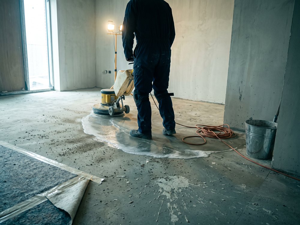 Einscheibenmaschine reinigt den Estrichboden eines Rohbaus; vor der Maschine liegt noch trockener Bauschmutz