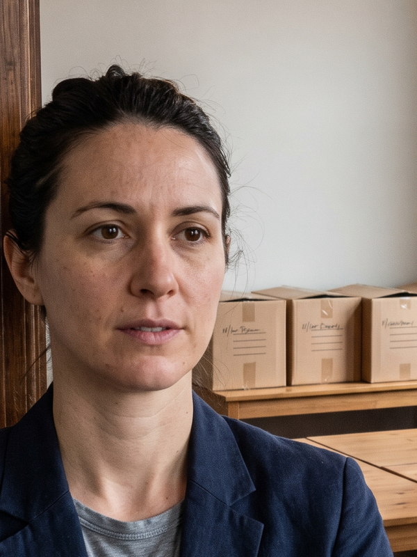 Eine Frau im marineblauen Blazer steht in der T&uuml;r eines eben bezogenen B&uuml;ros, dahinter zusammengeschobene Schreibtische und beschriftete Kartons