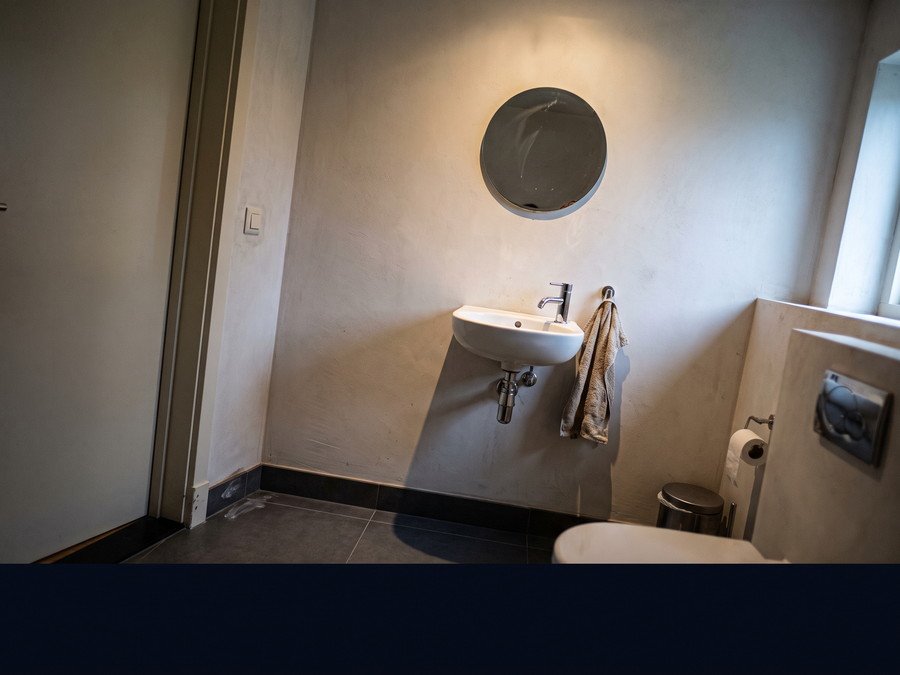 Fertiges G&auml;ste-WC mit schmalem Wandwaschtisch, rundem Spiegel, Wand-WC und dunklen Bodenfliesen