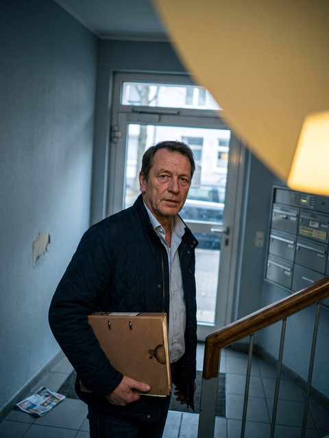 H. Terwiel im dunkelblauen Steppmantel mit einem Ordner unter dem Arm im Hausflur