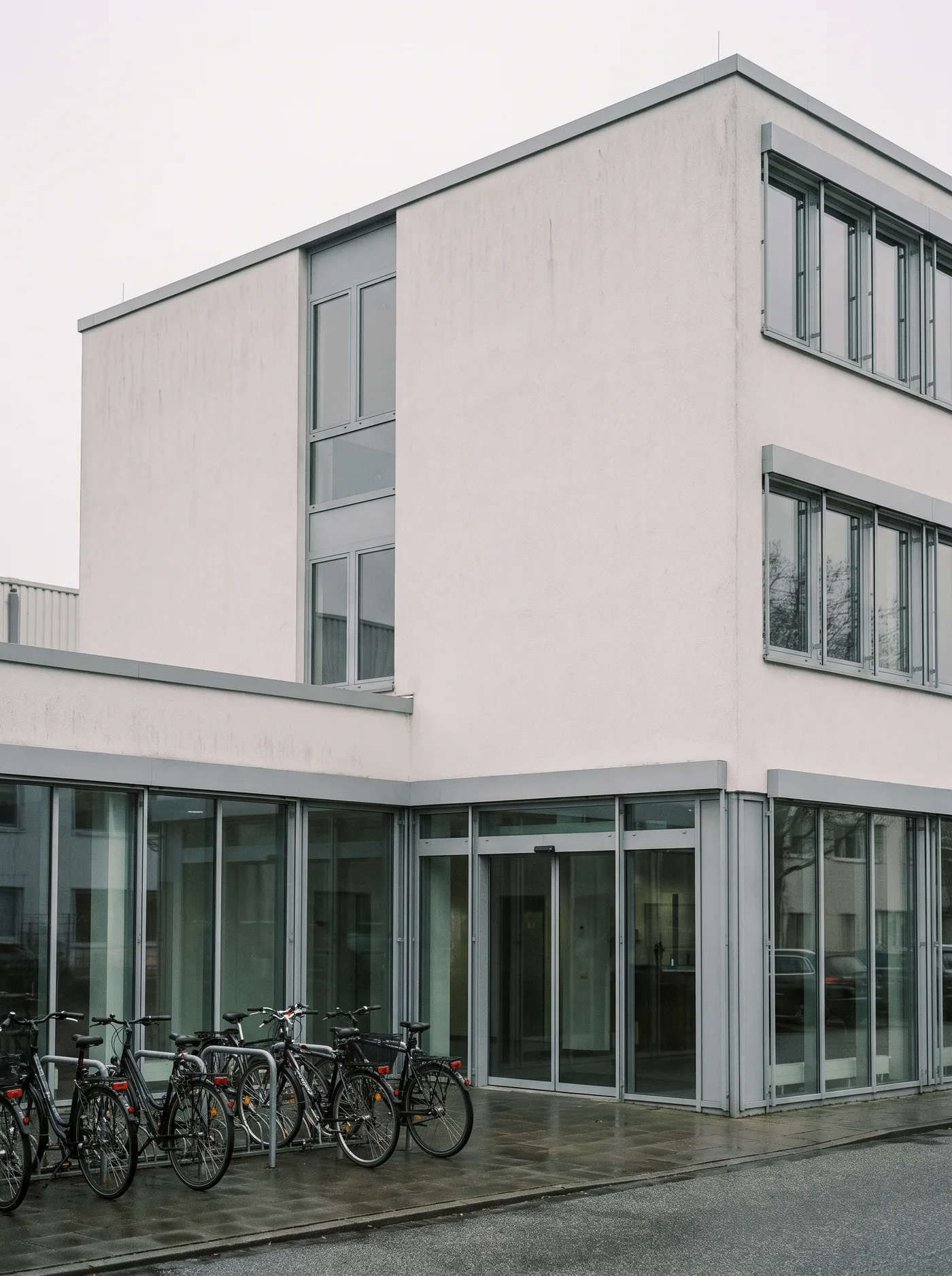 Weiß verputztes Praxisgebäude mit großen Fenstern und Glaseingang.