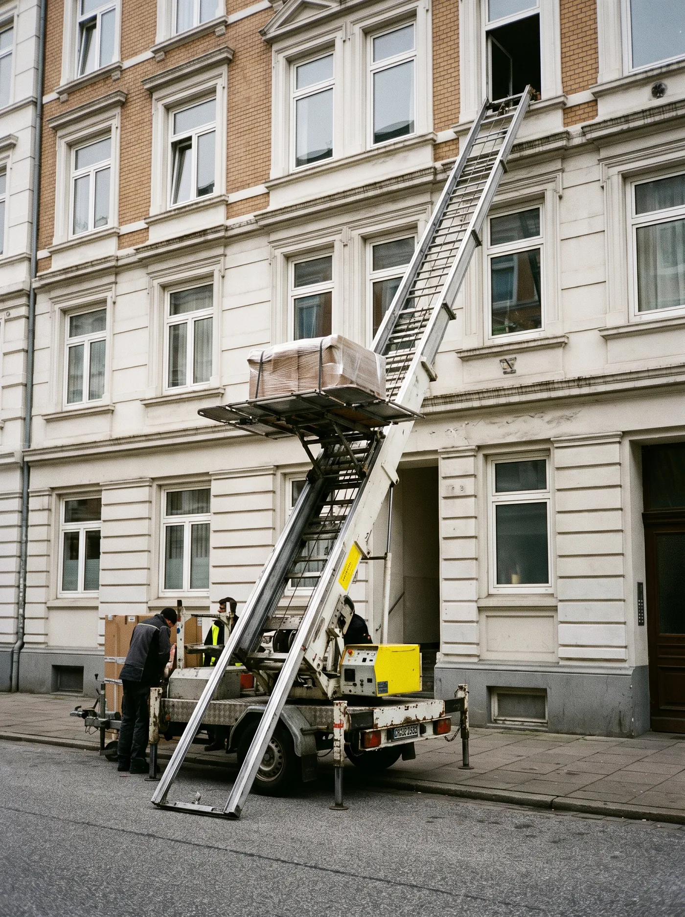 Ein Möbellift lehnt an der Fassade eines Hamburger Altbaus, von unten gesehen, die Plattform auf Höhe des vierten Stocks.