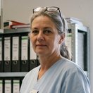 Sabine Kortmann im hellblauen Kasack vor dem Aktenregal