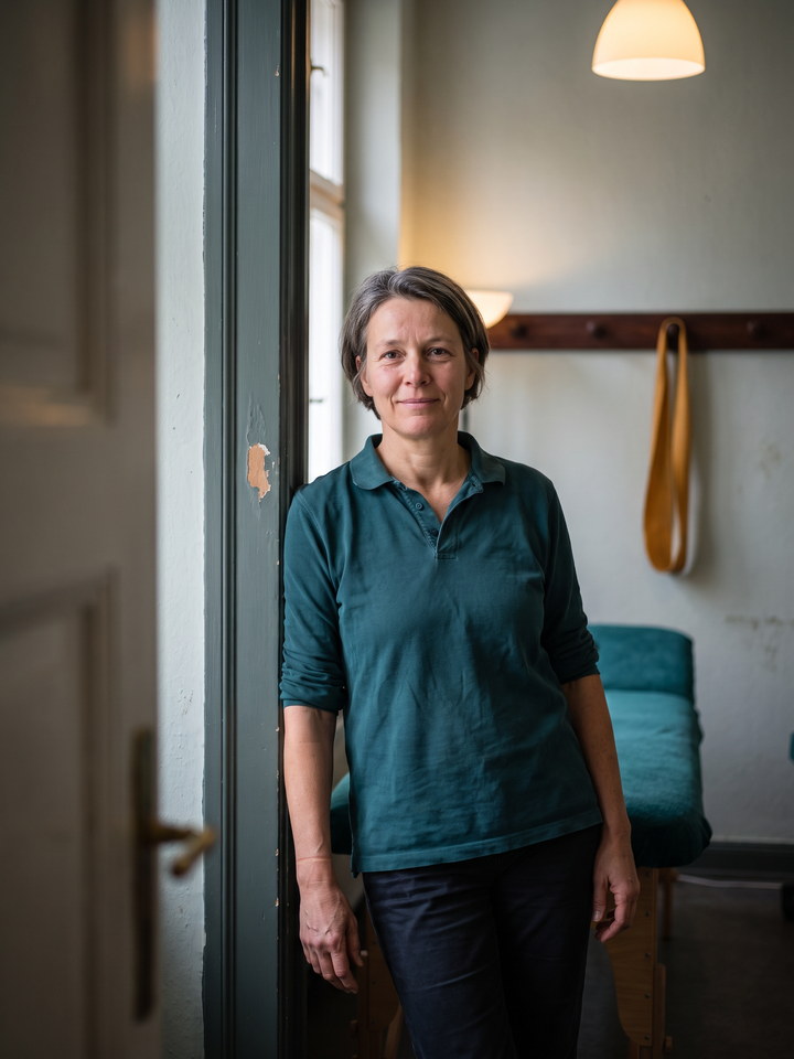 Andrea Bergmann, kurzes ergrautes Haar, im petrolfarbenen Poloshirt im offenen T&uuml;rrahmen eines Behandlungsraums