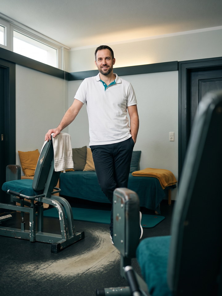 Tobias Klarhoff mit kurzem Bart im wei&szlig;en Poloshirt mit petrolfarbenem Kragen, eine Hand am Rahmen eines Trainingsger&auml;ts