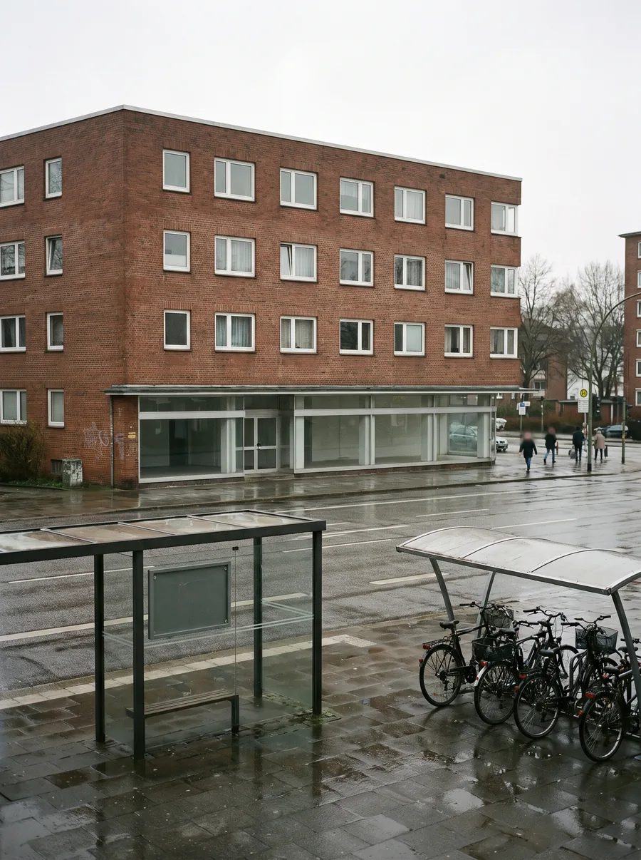 Vierstöckiger Klinkerbau an einer Hauptstraße in Barmbek, im Erdgeschoss eine Ladenzeile, davor eine Bushaltestelle und Fahrräder.