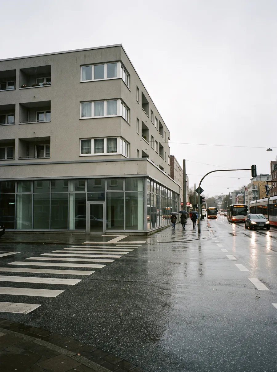 Heller Nachkriegsbau an einer breiten Kreuzung in Wandsbek, Glasfront im Erdgeschoss, Zebrastreifen im Vordergrund.