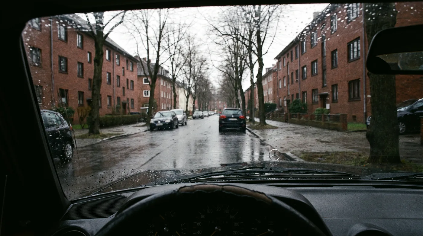 Blick durch die Windschutzscheibe eines Fahrschulwagens auf eine ruhige Hamburger Straße mit Backsteinhäusern bei Regen.