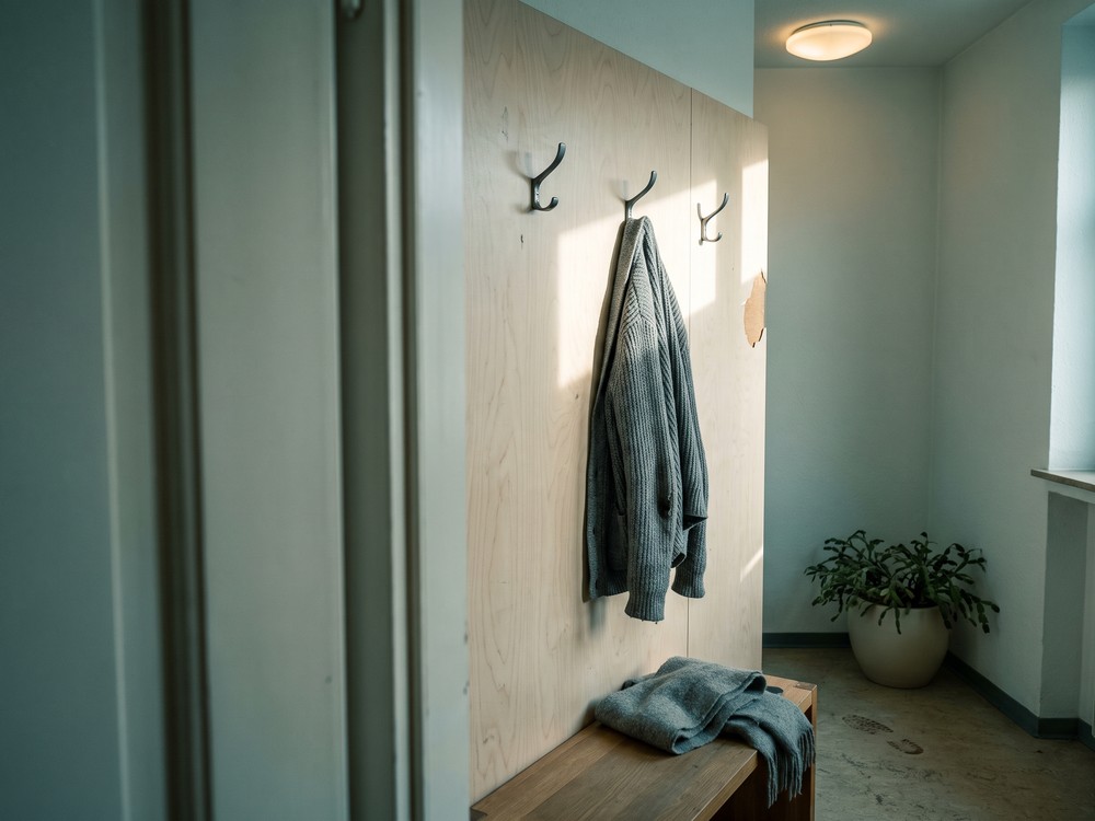 Flur der Praxis: drei Garderobenhaken an einer Birkenholzwand, an einem h&auml;ngt eine Strickjacke, darunter eine schmale Bank